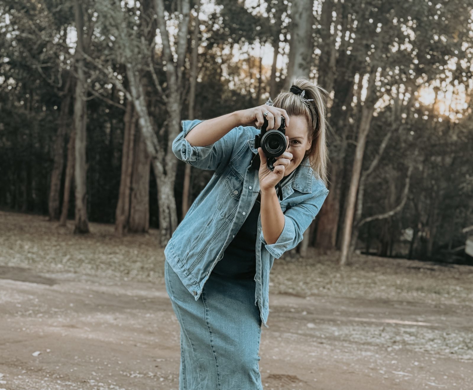 Elise in a denim jacket among gum trees, smiling behind her camera