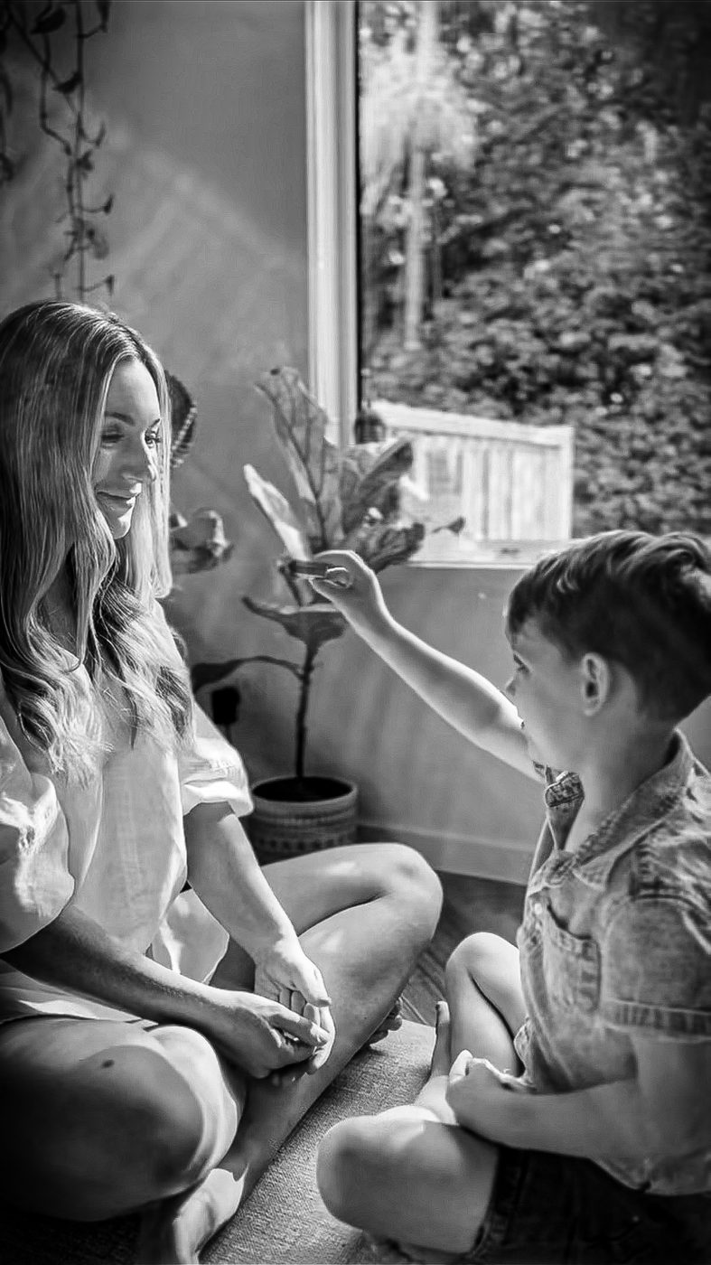 Elise sitting cross-legged at home as her son reaches toward her, in black and white