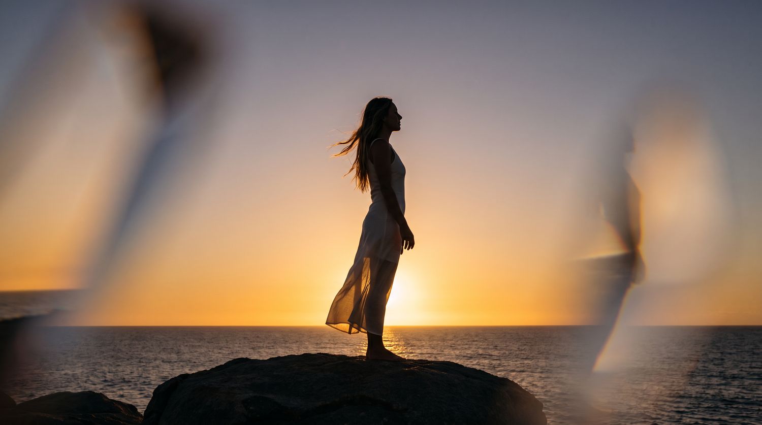 Silhouette of a woman standing on a rock at sunset